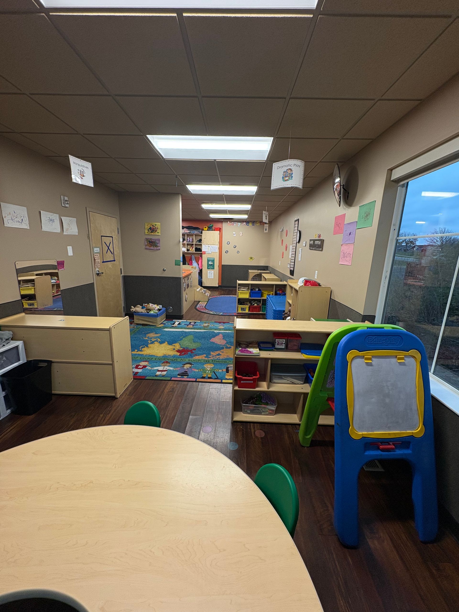 Childcare classroom interior with tables, play areas, and a window.