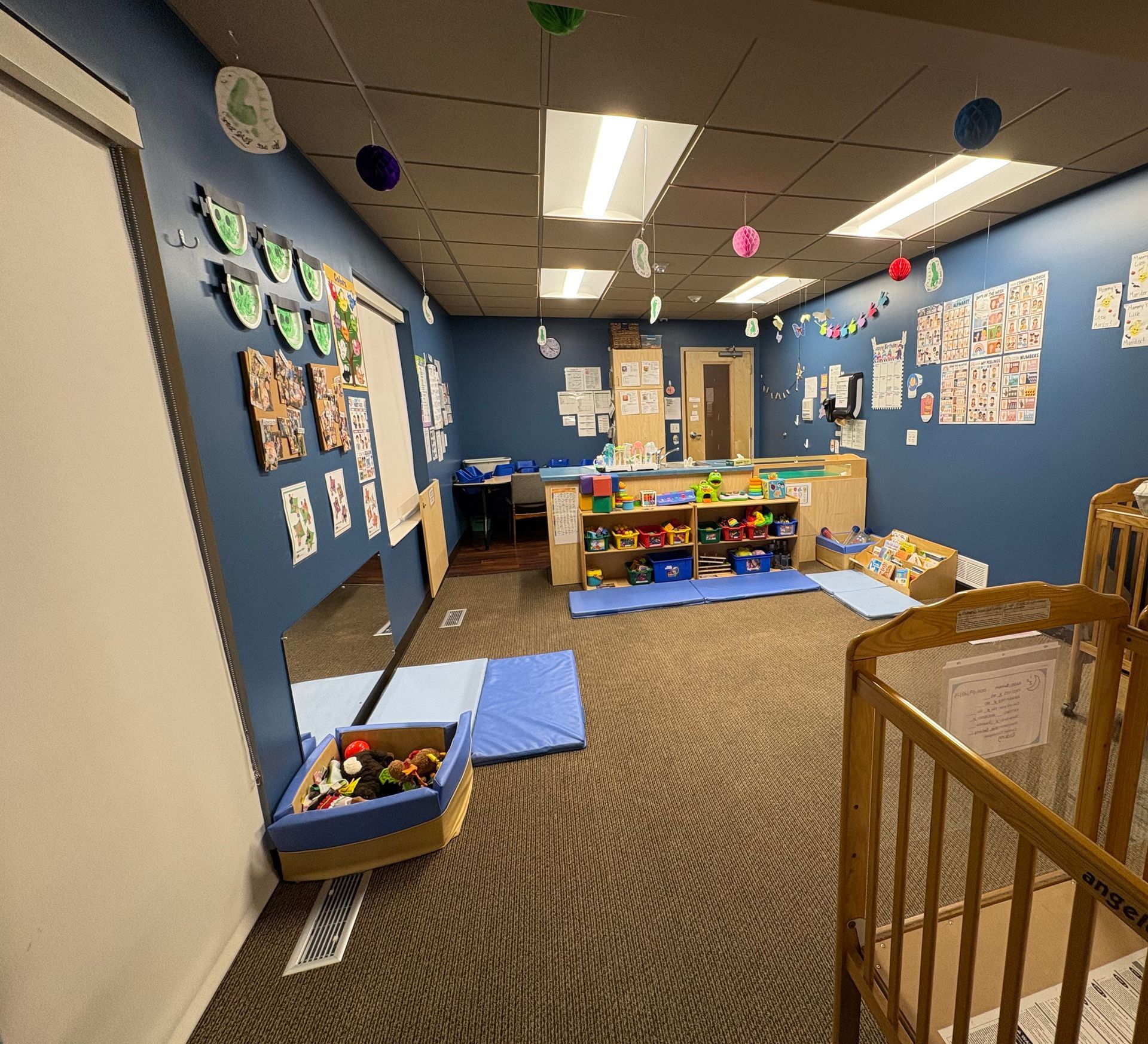 A children's playroom with blue walls, toys, and a crib. Colorful decorations hang from the ceiling.