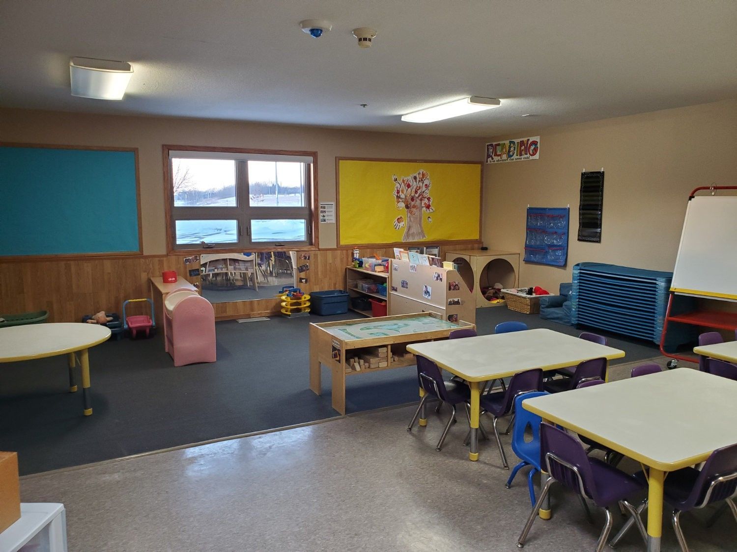 Empty preschool classroom with tables, toys, and bulletin boards.