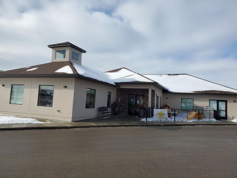Exterior of a building with snow on the roof. It has a central entrance, and cloudy skies overhead.