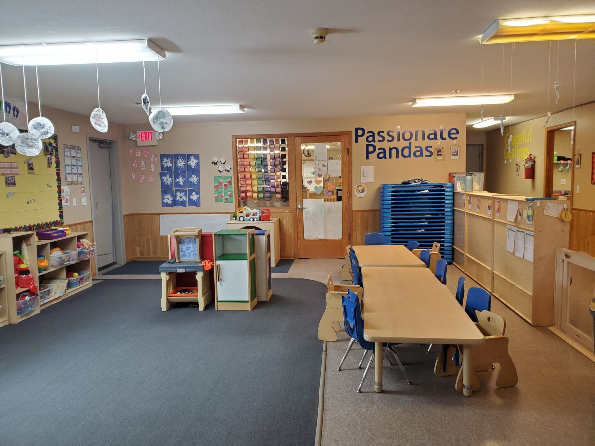 Empty classroom: tables, chairs, play kitchen, storage, and Panda-themed door.
