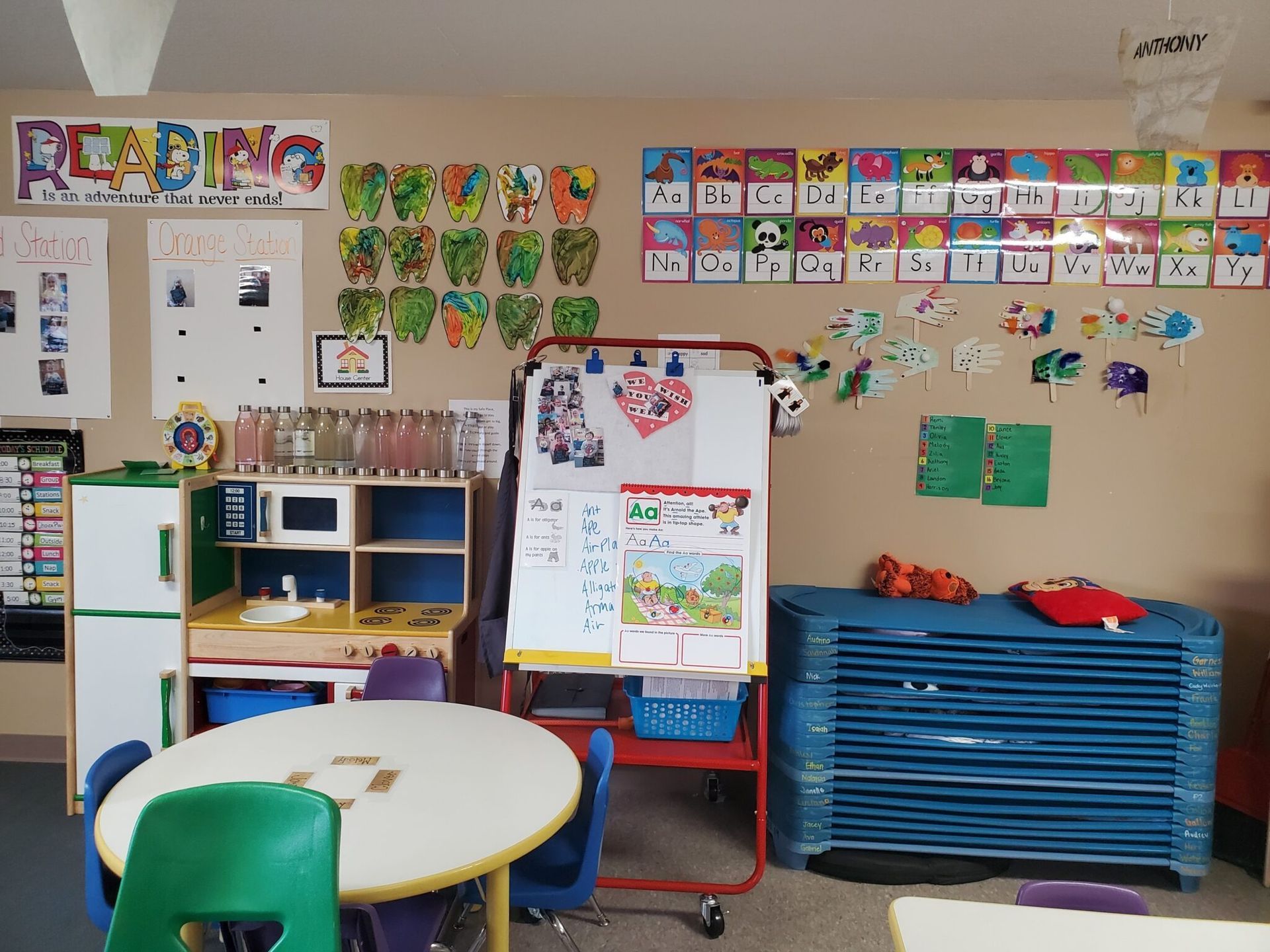 Classroom with a white board, play kitchen, colorful decorations, and round table with chairs.