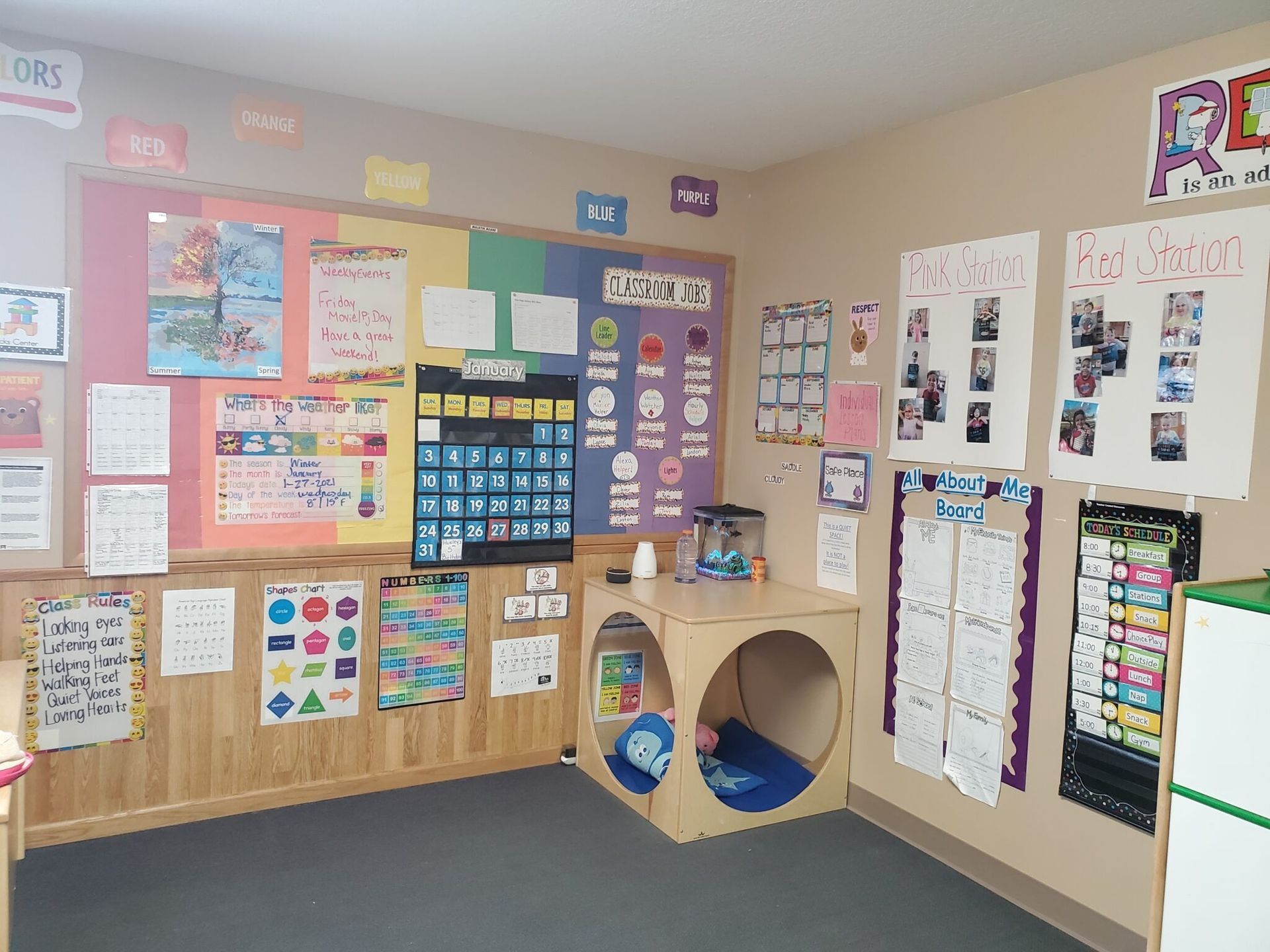 Classroom corner with learning charts, calendar, and a wooden play cube.
