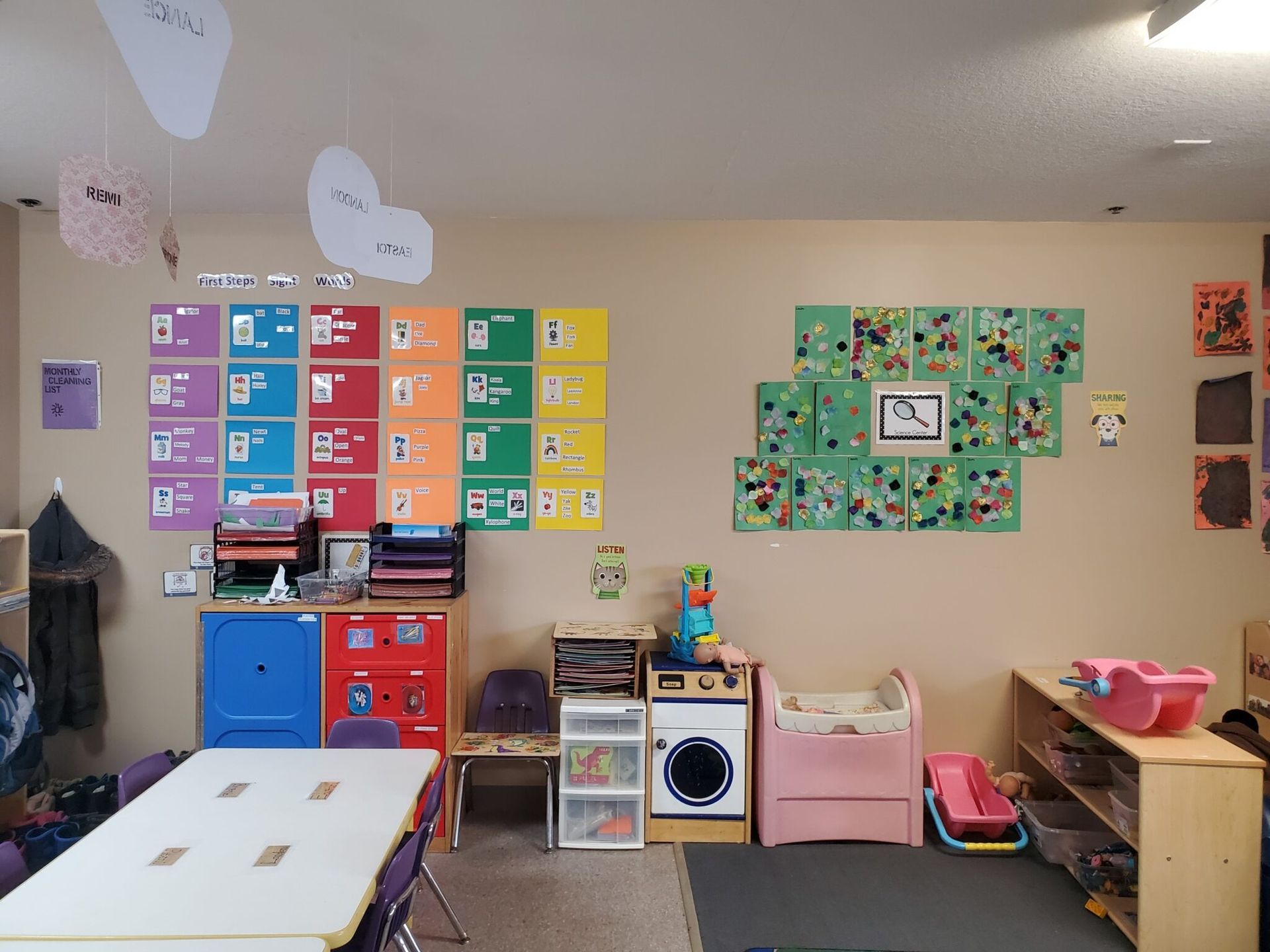 Interior of a colorful preschool classroom. Walls have educational posters. Furniture includes tables, chairs, and storage units.