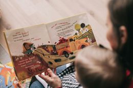 Woman reading a children's book to a toddler, featuring colorful illustrations of a truck on a farm.
