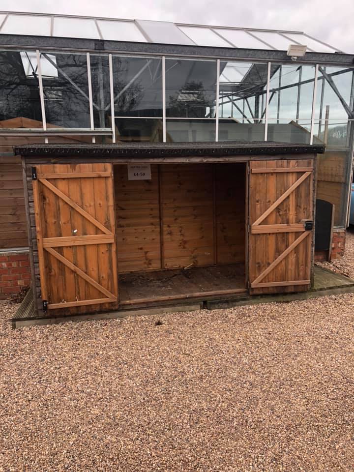 a wooden shed with a greenhouse in the background .