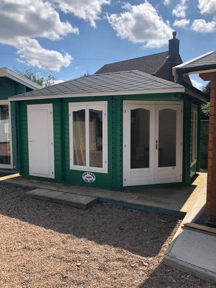 A green house with white doors and windows is sitting on top of a gravel lot.