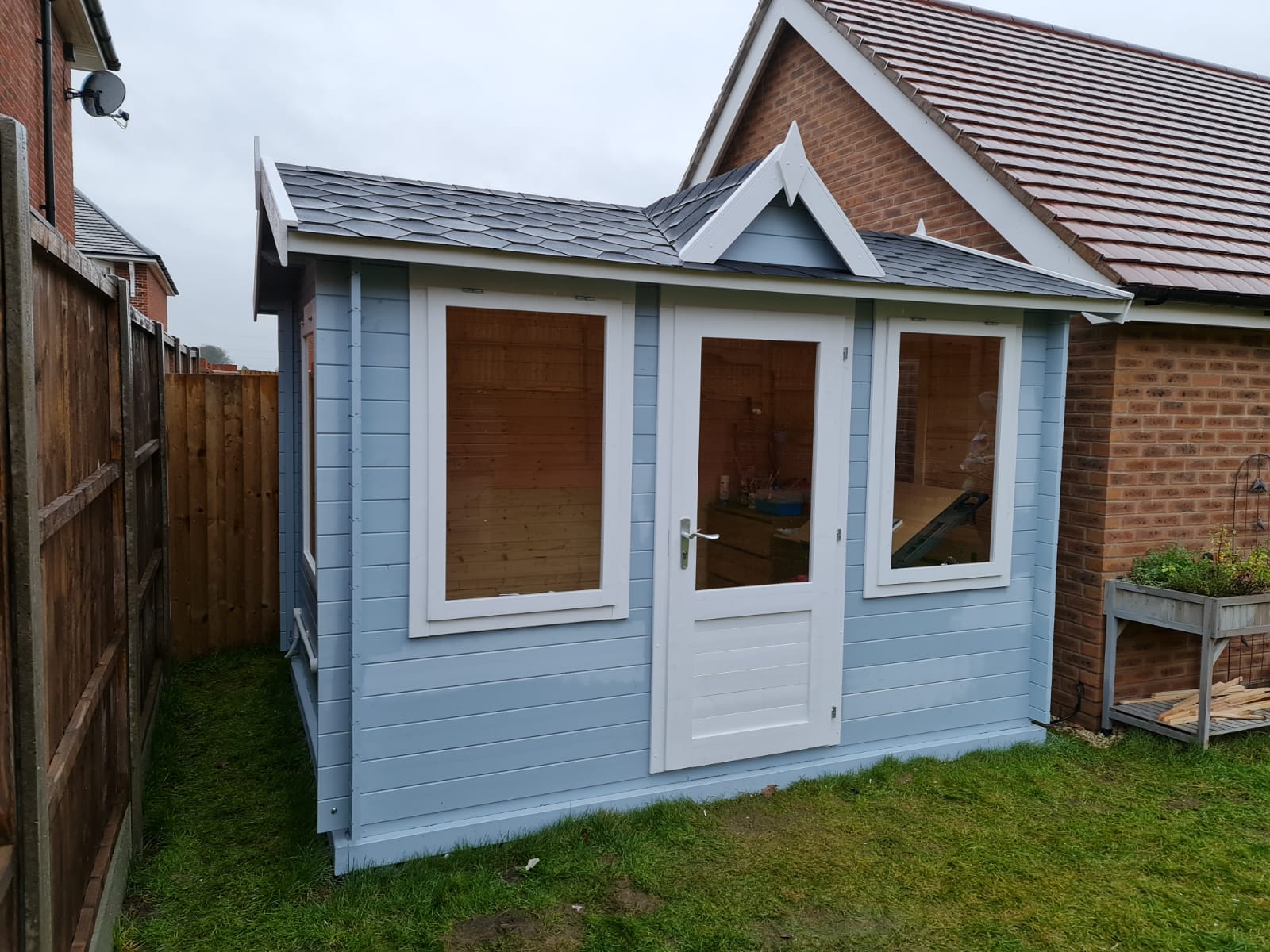 A small blue and white house is sitting in the grass in front of a brick house.