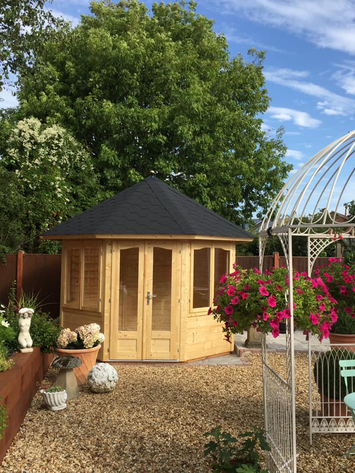 A wooden gazebo with a black roof is sitting in the middle of a gravel yard.