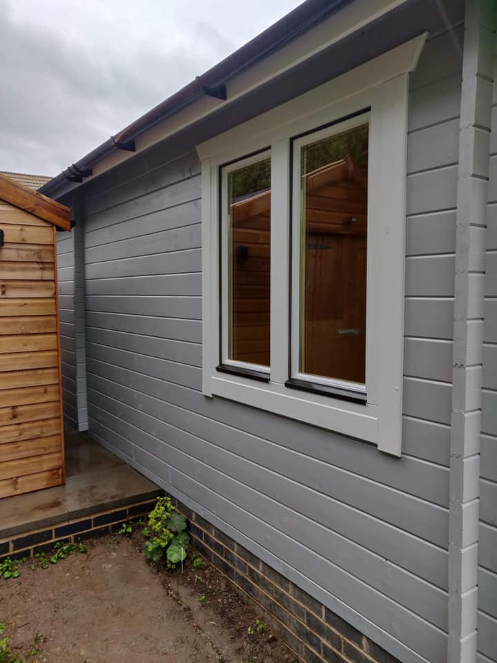 The side of a house with two windows and a wooden shed.
