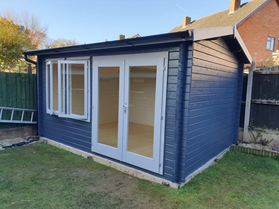A blue wooden cabin with white doors and windows in a backyard.