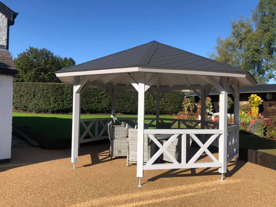 a white gazebo with a black roof is sitting in the middle of a garden .