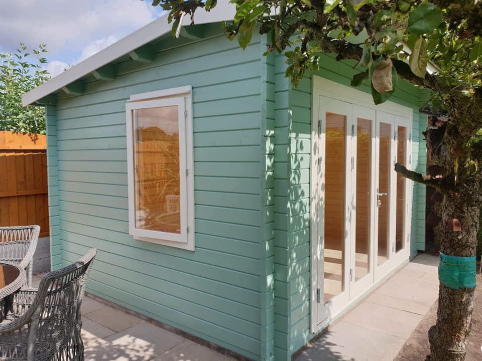 A small green house with a lot of windows and doors.