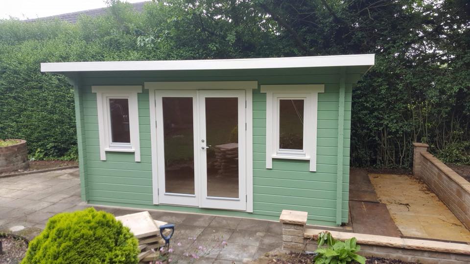 A green wooden house with white trim is sitting in the middle of a garden.