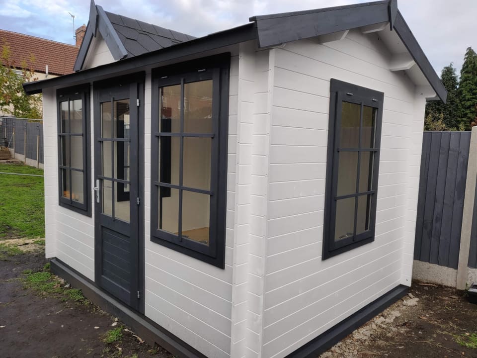 A white and black wooden house with a fence in the background.