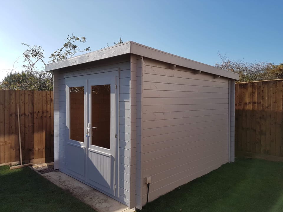 A small white wooden shed in a backyard next to a wooden fence.