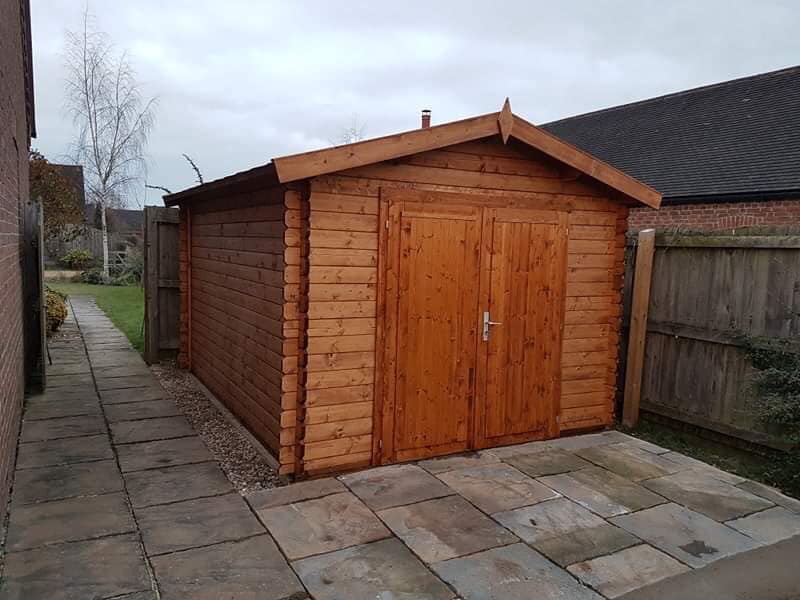 A wooden shed is sitting on a sidewalk next to a house.