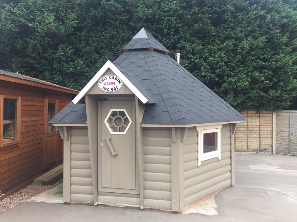 A small wooden house with a black roof is sitting in a parking lot.