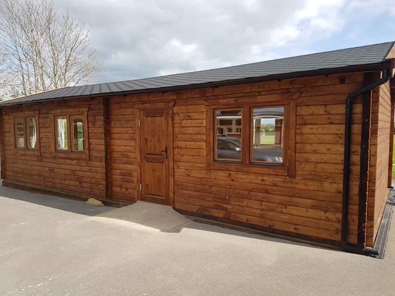 A long wooden building with a black roof and a lot of windows.