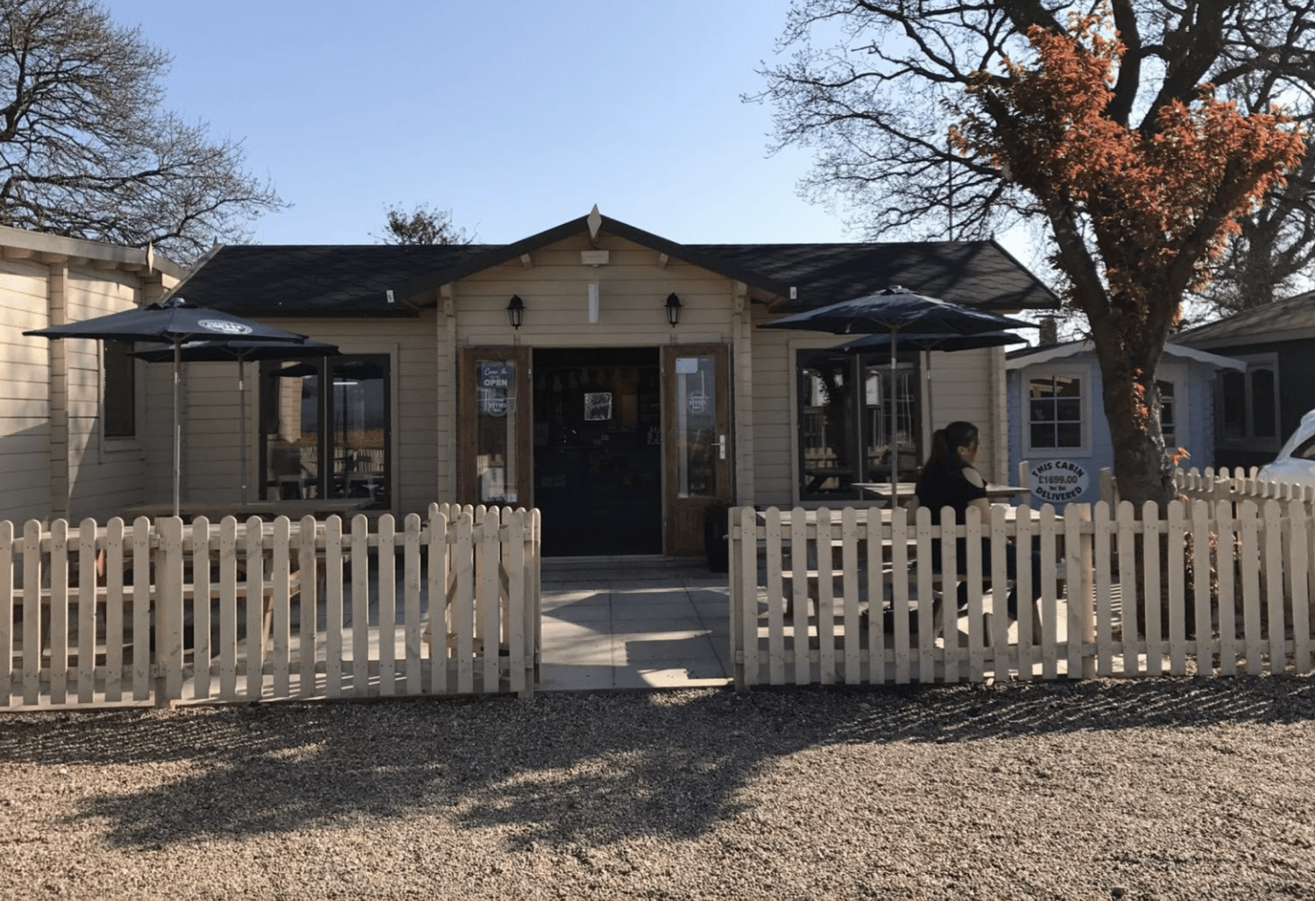A white picket fence surrounds a house with umbrellas in front of it.