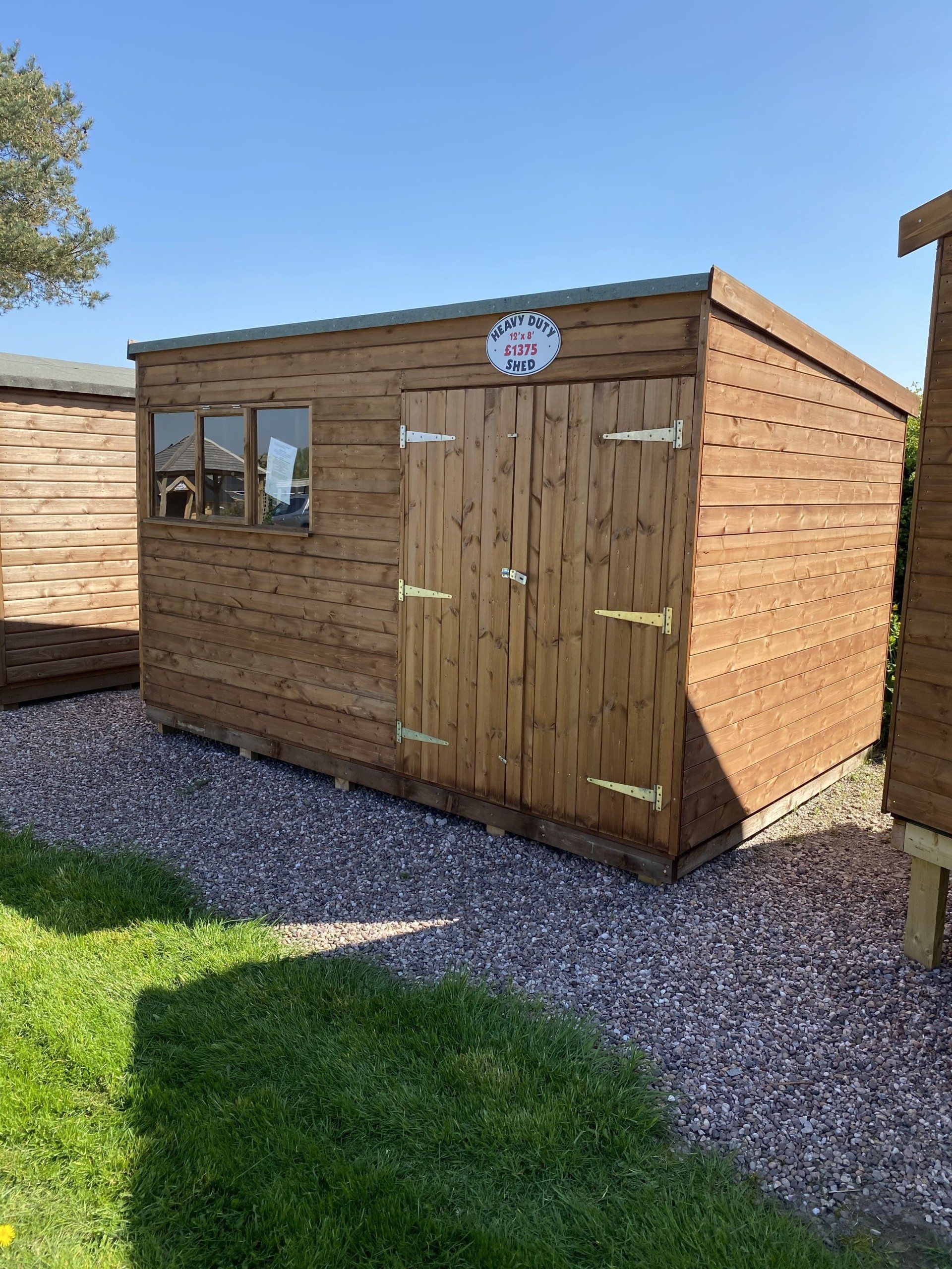 A wooden shed is sitting in the middle of a gravel driveway.