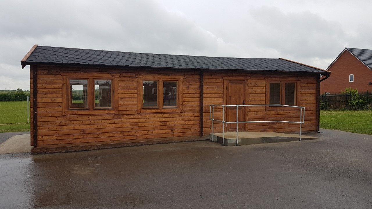 A small wooden house with a handicap ramp is sitting in the middle of a field.