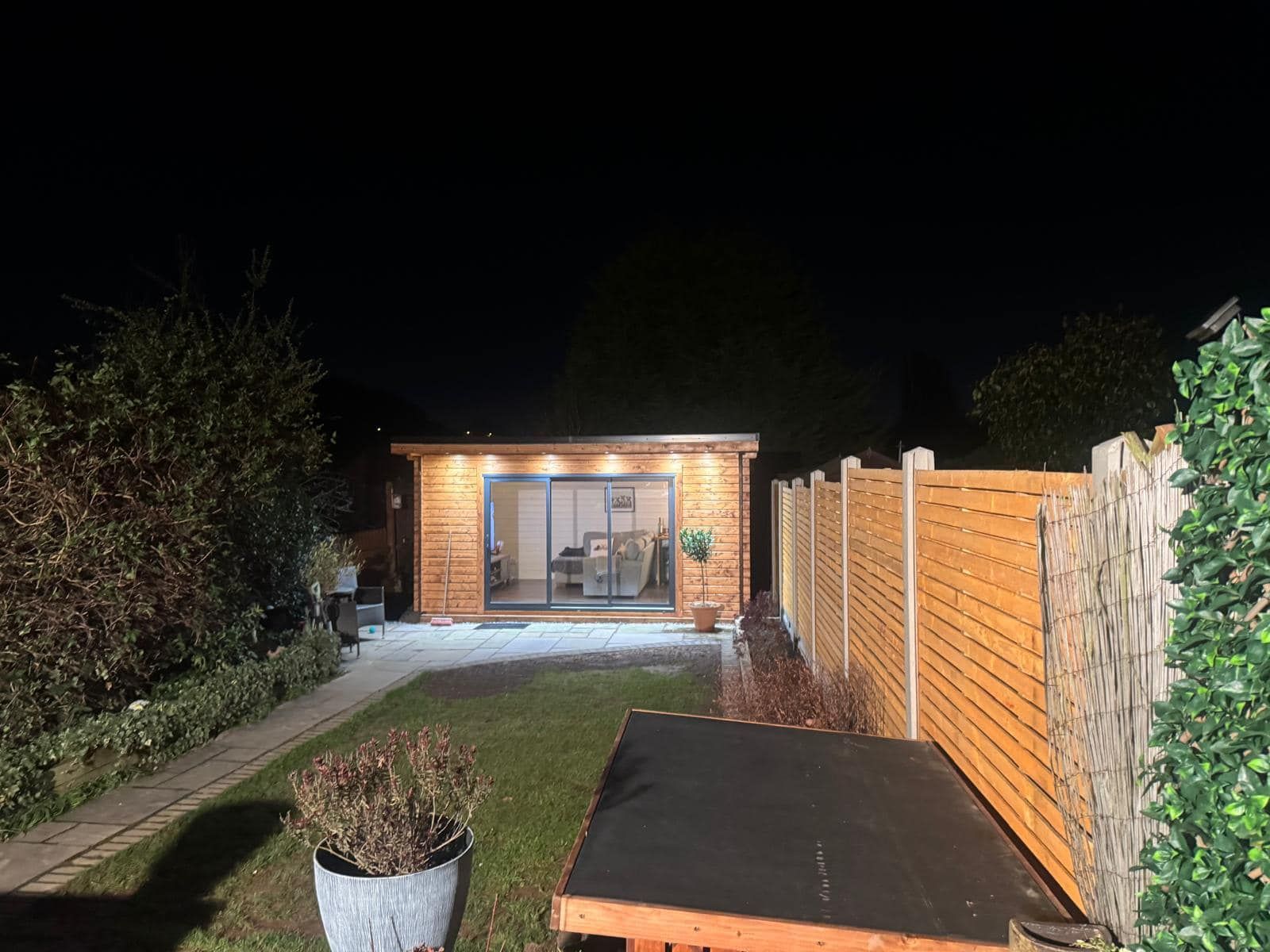 A wooden house is lit up at night in a backyard.