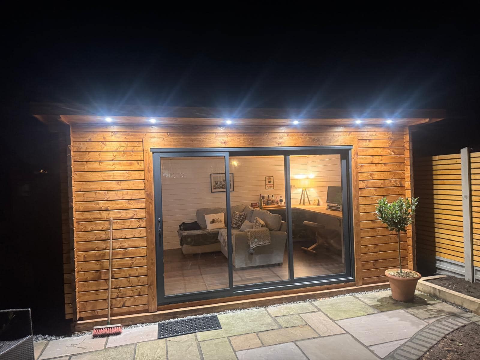 A wooden house with sliding glass doors and a living room at night.