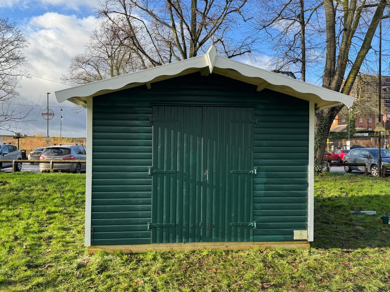 A green shed with a white roof is sitting in the middle of a grassy field.