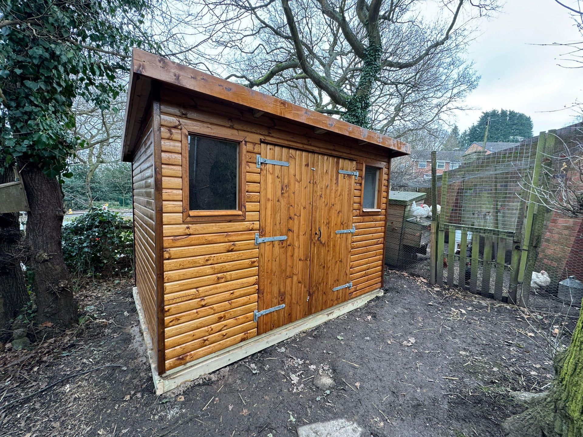 A wooden shed is sitting in the middle of a dirt yard.