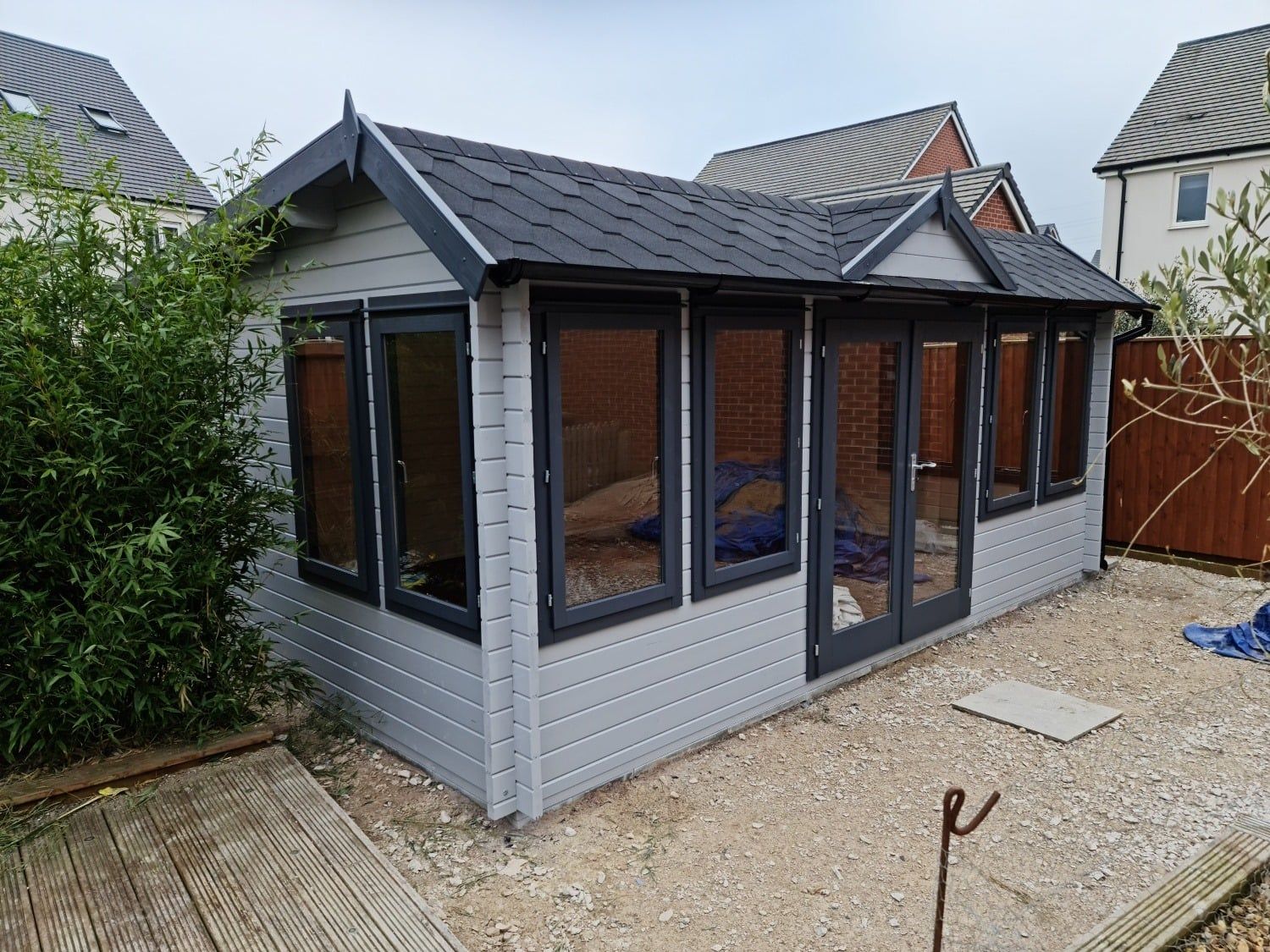A small house with a roof and a lot of windows is sitting in a gravel yard.
