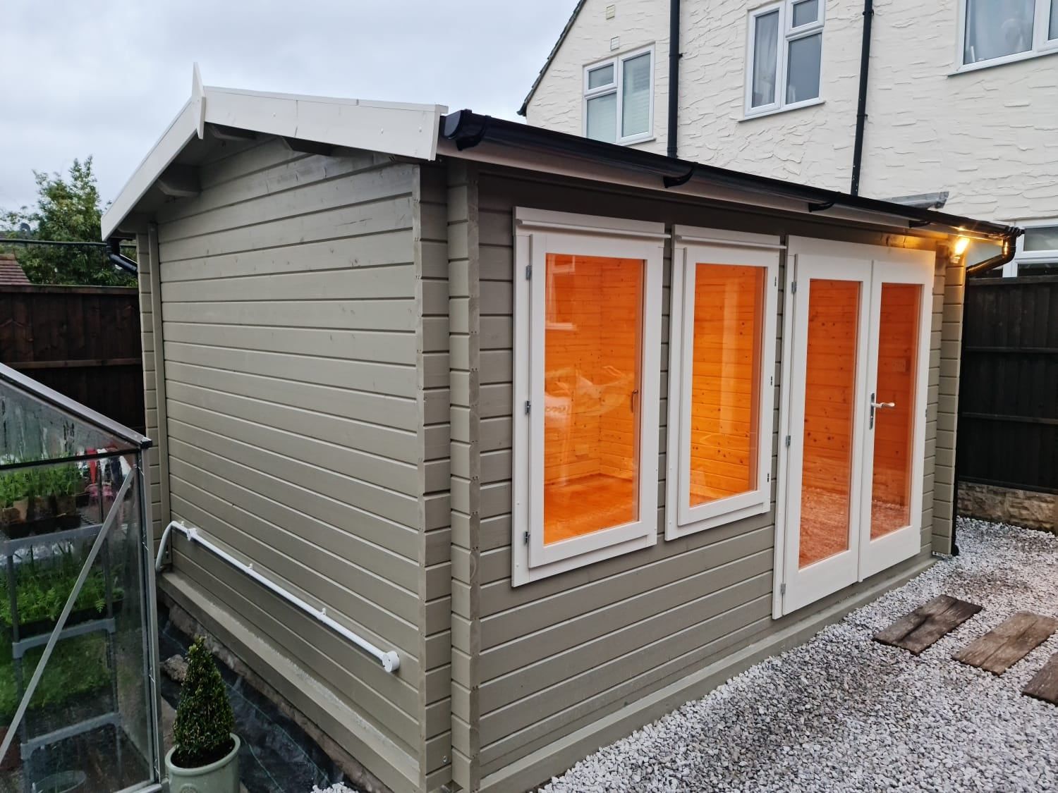 A small wooden house with orange windows and doors is in the backyard of a house.