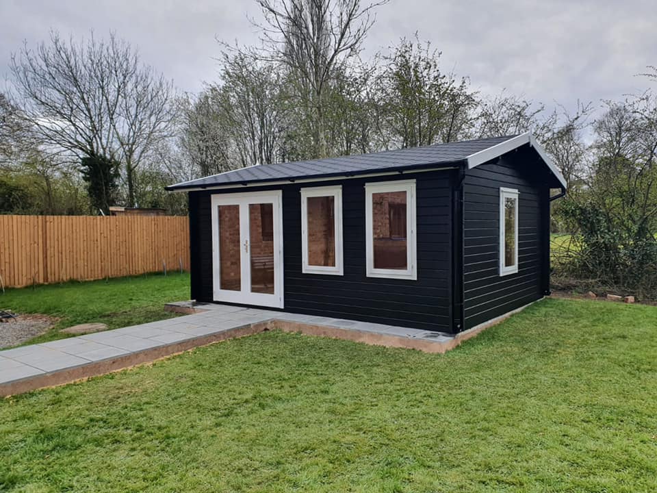 A black shed with white windows is sitting in the middle of a lush green yard.