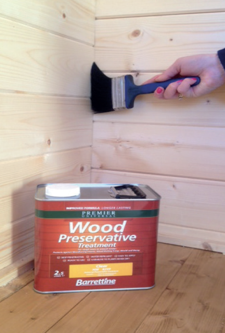 A person is applying wood preservative treatment with a brush