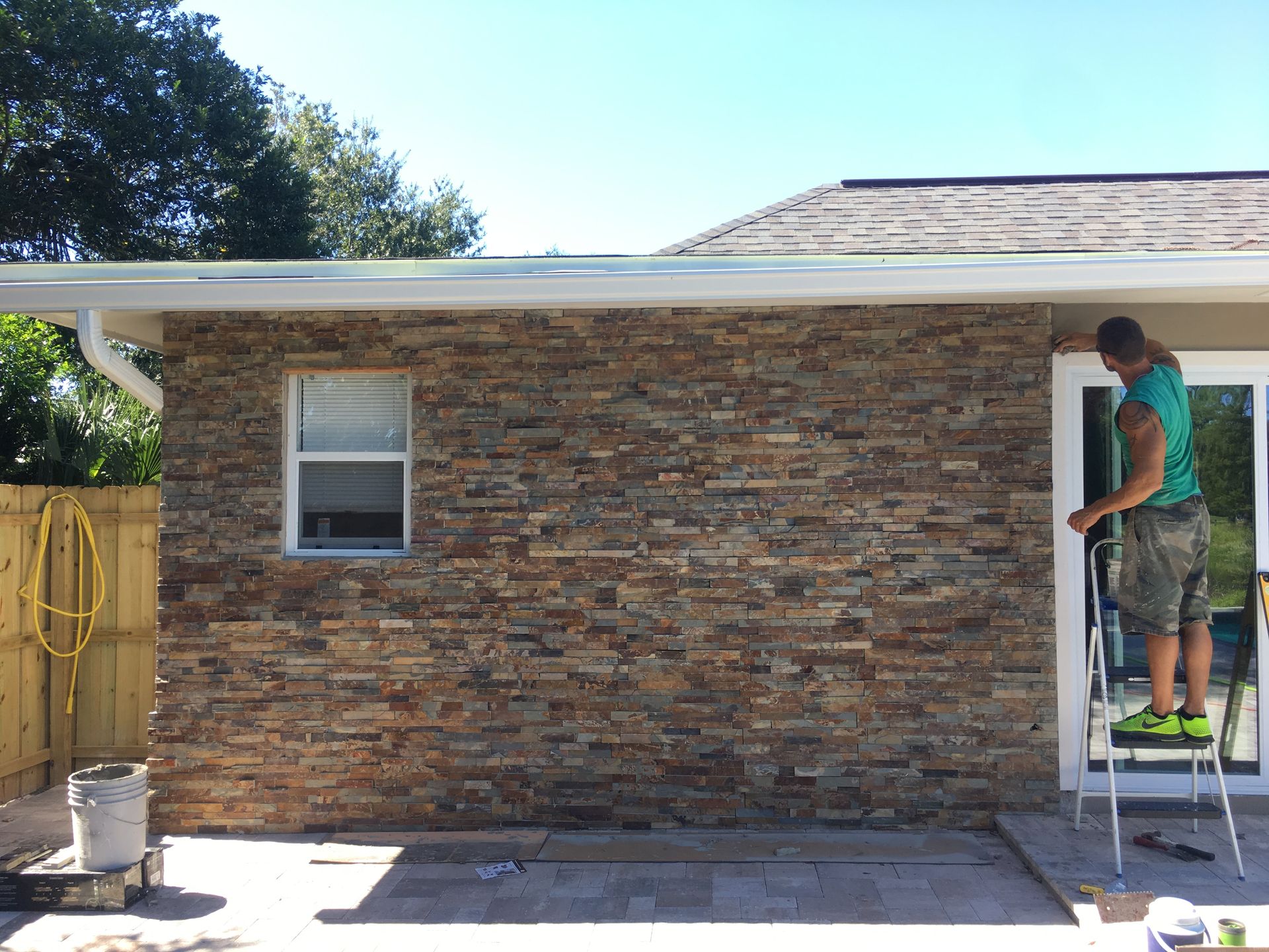 A man is standing on a ladder in front of a brick house.