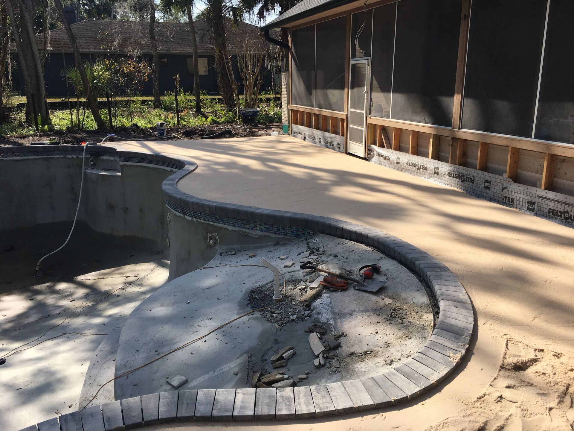 A swimming pool is being built next to a screened in porch.