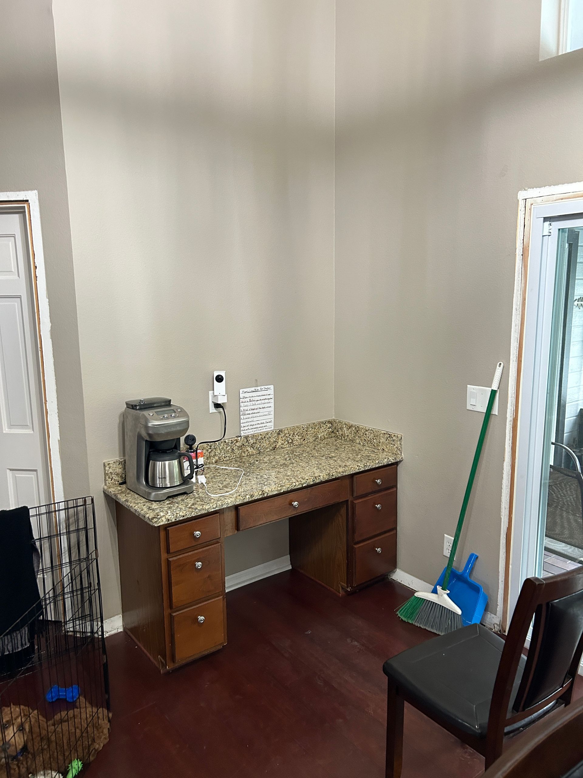 A room with a desk , chair , coffee maker and broom.
