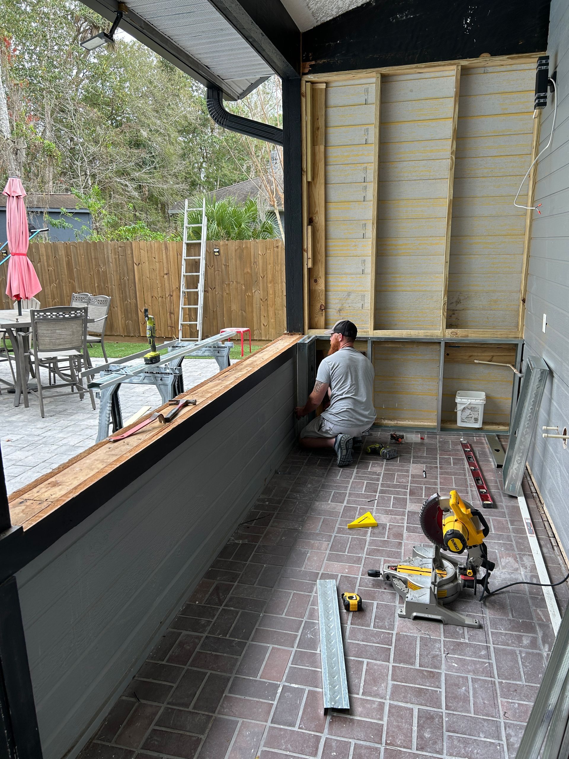 A man is kneeling on a porch working on a wall.