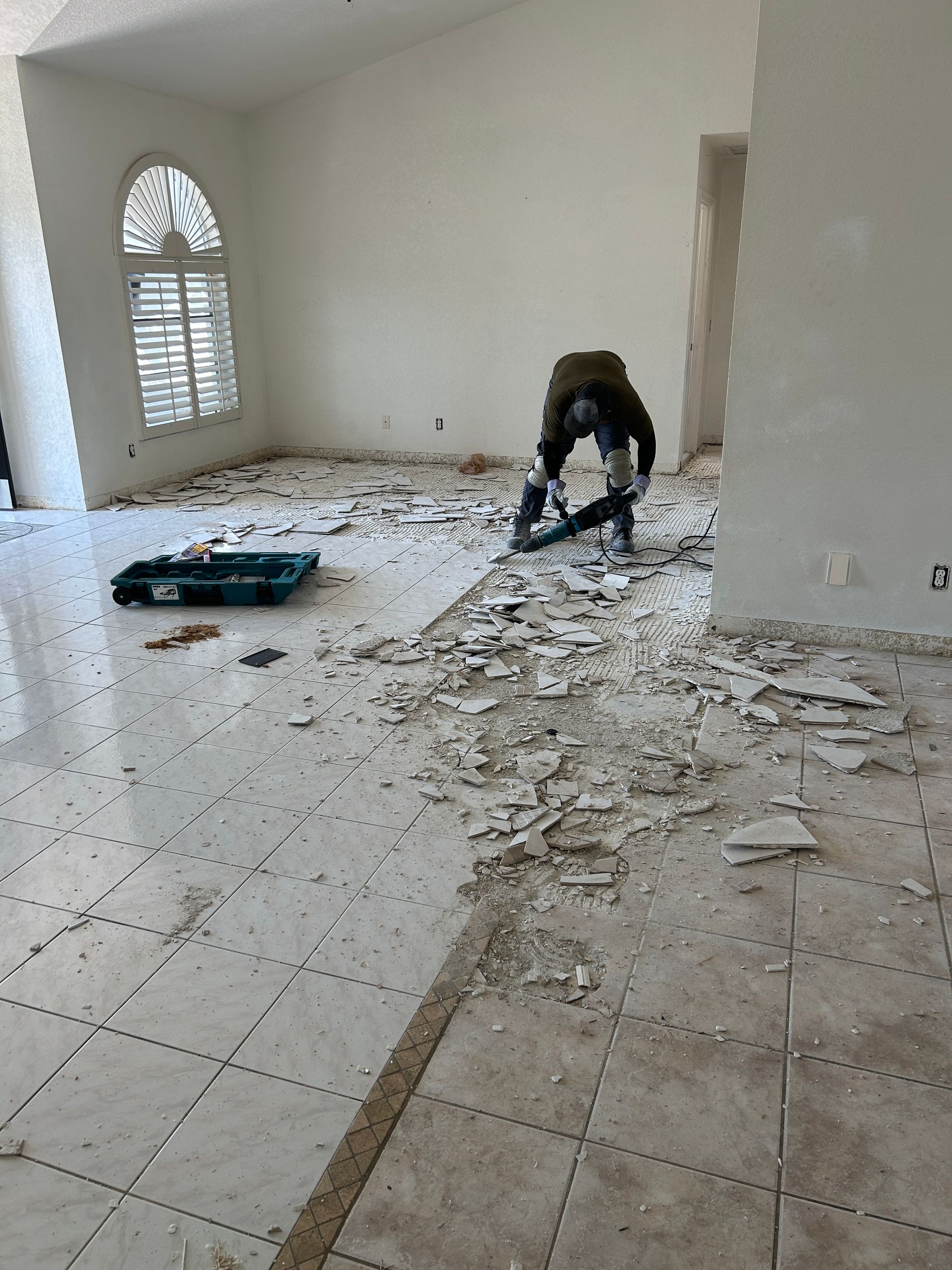 A man is working on a tile floor in an empty room.