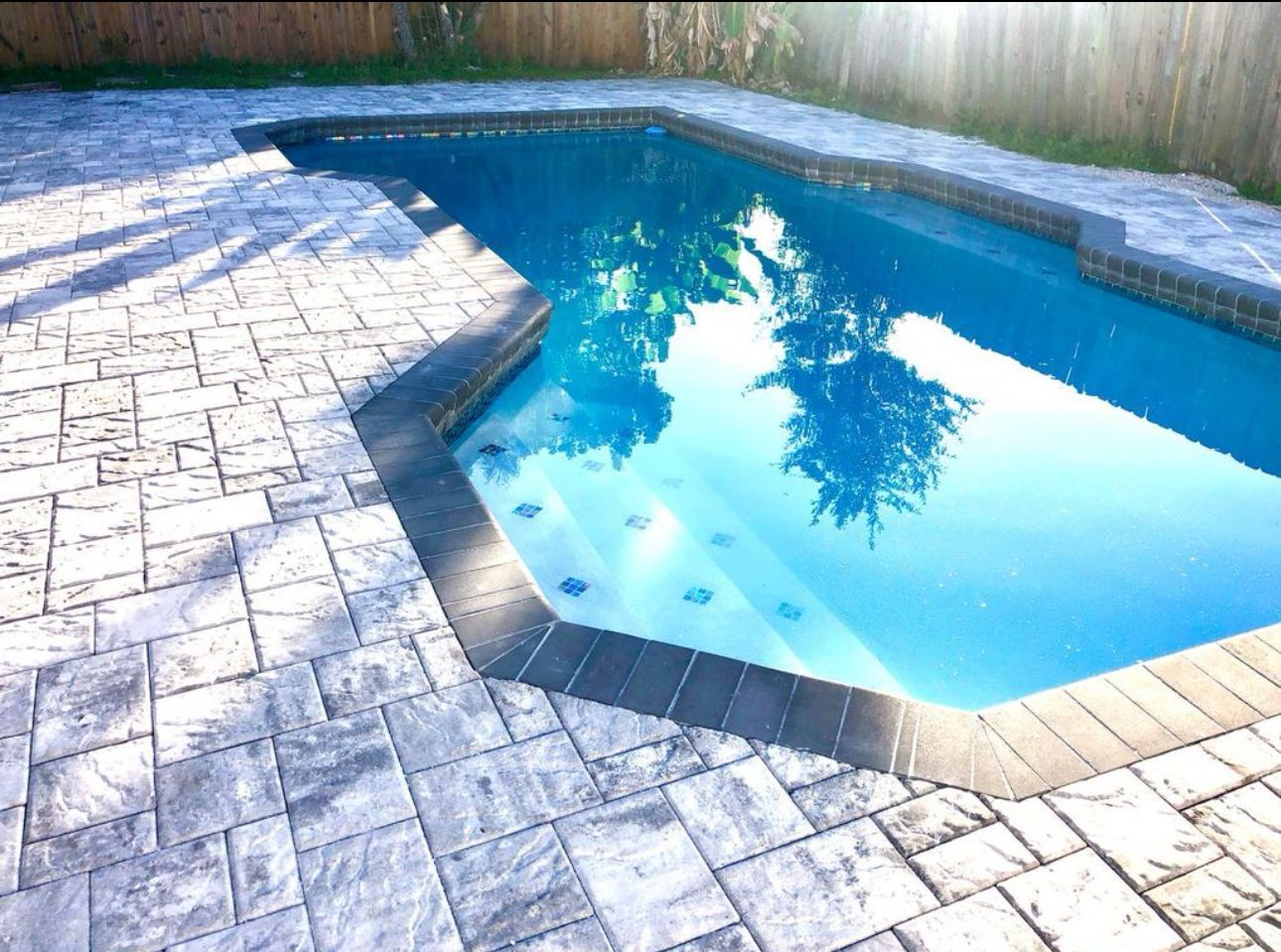 A large swimming pool is surrounded by a brick patio
