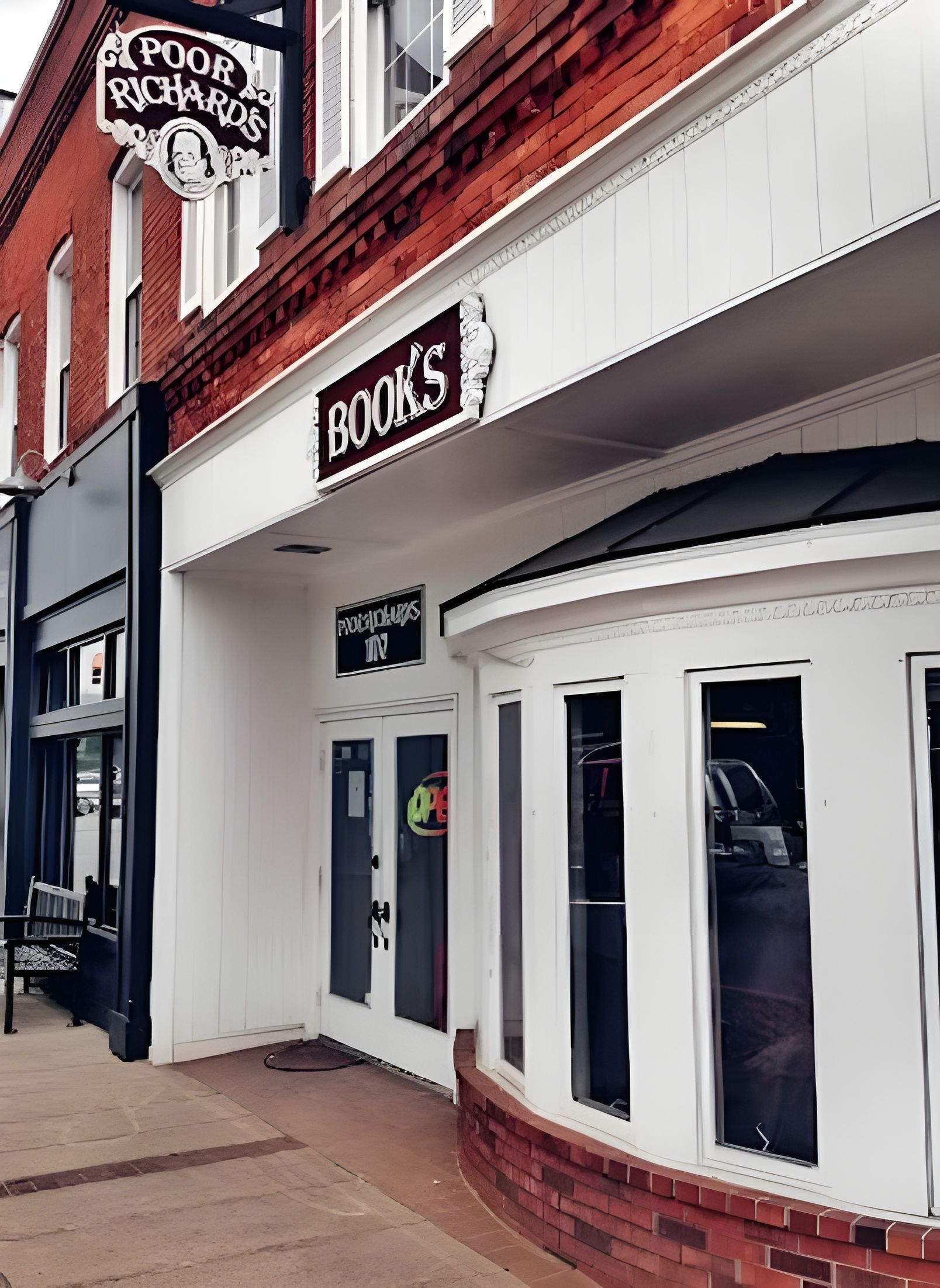 The storefront of Poor Richard's Books, a red brick building with white trim, hanging sign, and glass-paned entrance.
