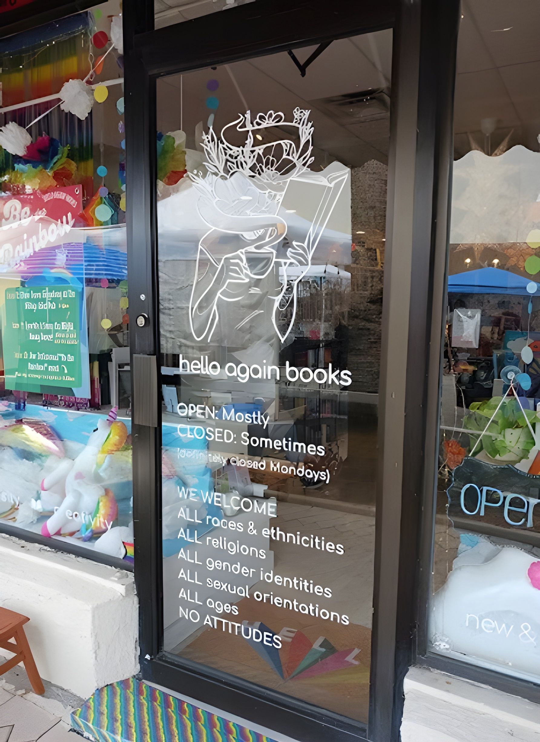 Glass door of Hello Again Books, featuring a logo, business hours, and a welcoming sign for all identities and backgrounds.