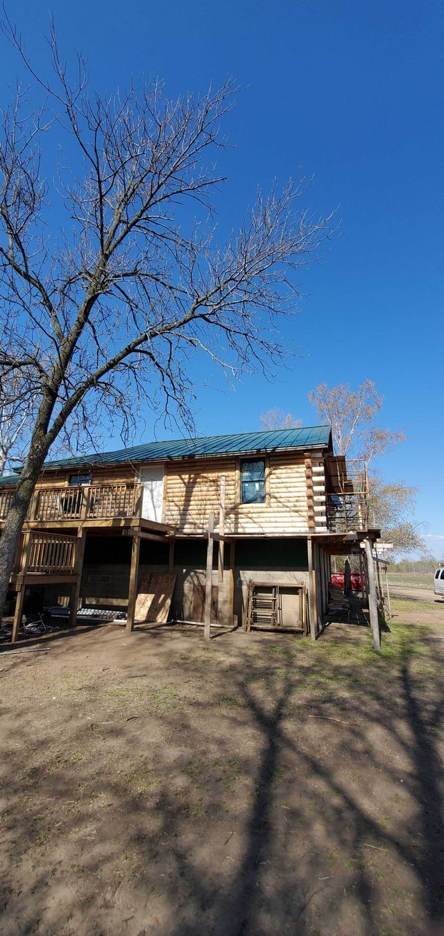 A log cabin is sitting on top of a dirt field next to a tree.