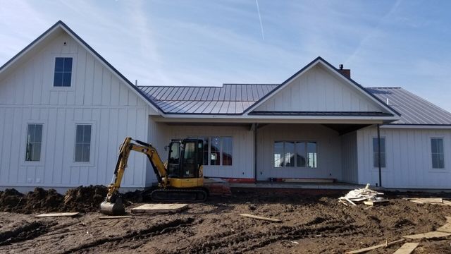 A yellow excavator is parked in front of a white house under construction.