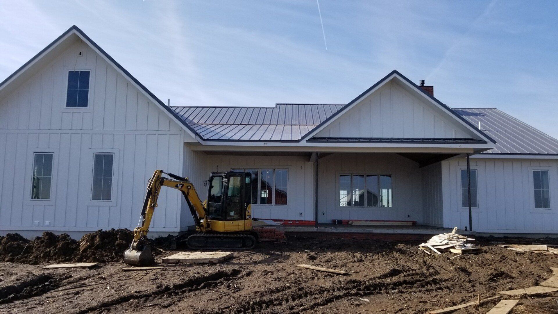 A yellow excavator is parked in front of a white house under construction.