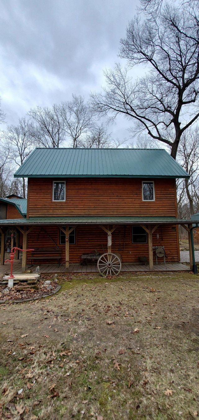 A log cabin with a green roof and a wagon on the porch.