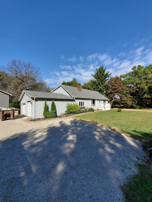 A white house with a gray roof is sitting on top of a lush green field.