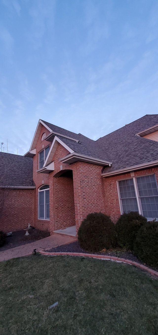 A large brick house with a gray roof is sitting on top of a lush green lawn.