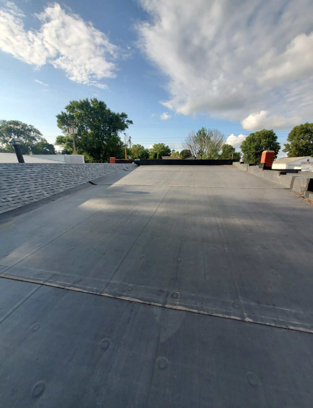 A rooftop with trees in the background and a blue sky with clouds.