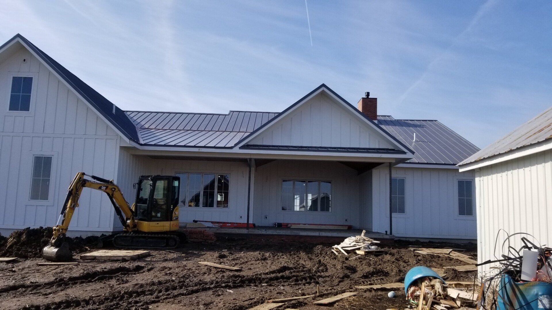 A large white house is being built with a yellow excavator in front of it.